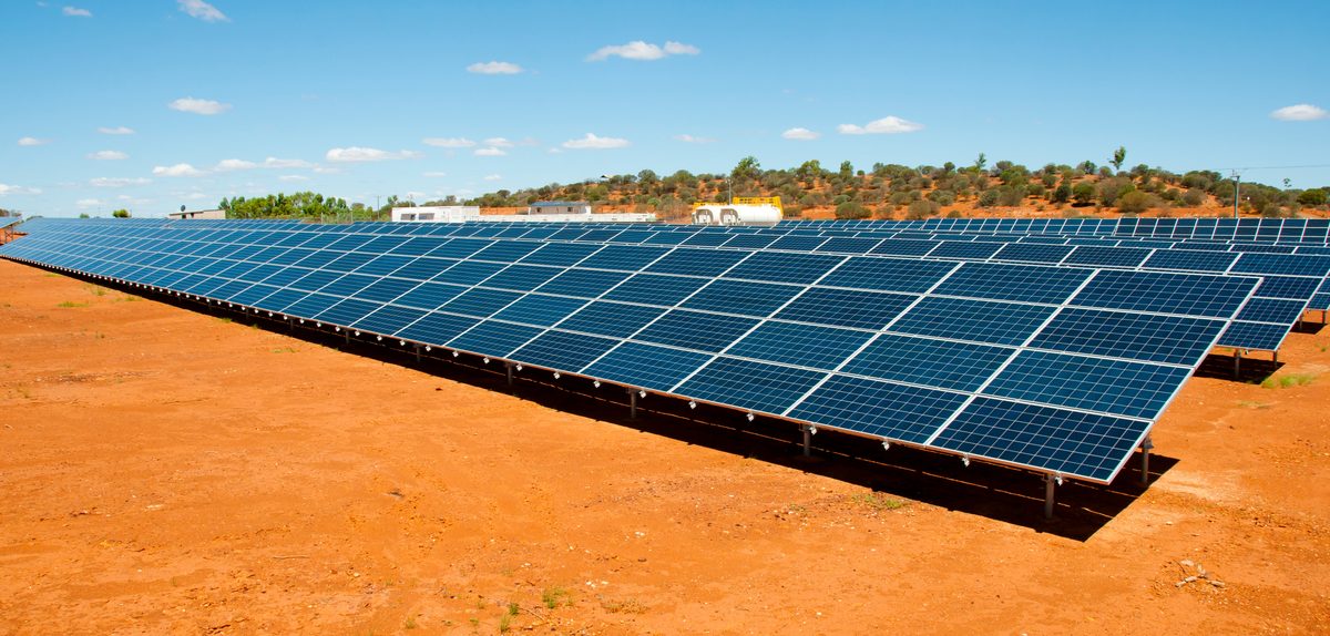 Rows of solar panels on red soil under a clear sky