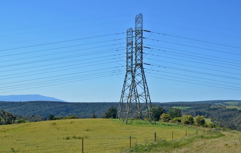 Transmission towers on a ridge above grazing country, with ranges beyond